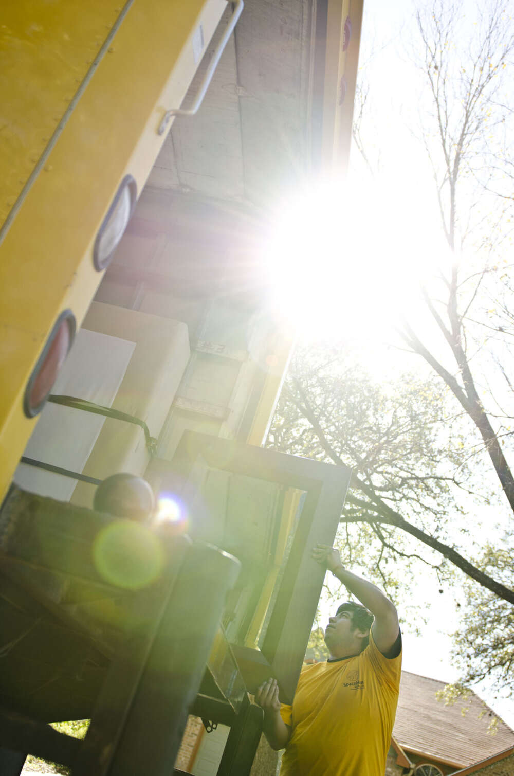 SpaceMan movers loading household items into the truck with sun flaring through Austin trees