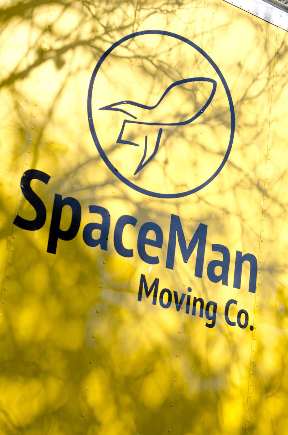 Close-up of the SpaceMan Moving Co. rocket logo on the truck with tree shadows